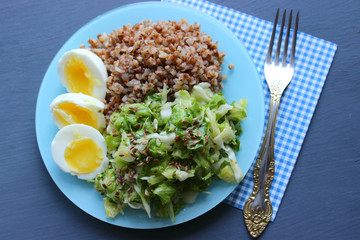 Buckwheat with vegetables. On a wooden background. The view from the top. Copy space. Healthy Breakfast with egg, salad and buckwheat porridge on a dark background. Proper diet. Diet menu.