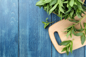 Mint. Leaves and branches of fresh green wild mint on a cutting board on a wooden blue table. top view. space for text