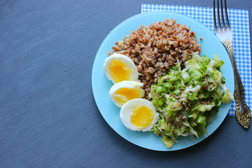 Buckwheat with vegetables. On a wooden background. The view from the top. Copy space. Healthy Breakfast with egg, salad and buckwheat porridge on a dark background. Proper diet. Diet menu.