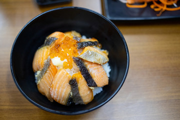 Grilled salmon with eggs topping on rice in black bowl