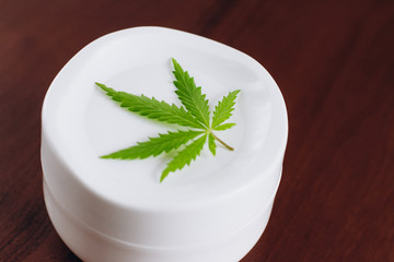 Macro close up of jar of cream from biological and ecological plants of hemp vegetable pharmaceutical oil CBD with green cannabis leaf with copy space