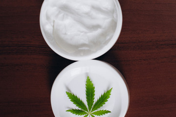 Macro close up of jar of cream from biological and ecological plants of hemp vegetable pharmaceutical oil CBD with green cannabis leaf with copy space