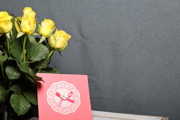 A bouquet of yellow roses and a greeting card. On a gray background.