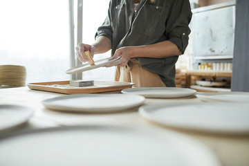 Mid secion portrait of unrecognizable young woman sanding handmade ceramic bowl in pottery workshop, copy space