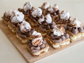 Portion cakes of meringue and cocoa butter cream in square form on a wooden stand, a piece of cake on a light wooden background. Restaurant serving. Selective focus, close up