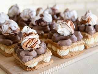 Portion cakes of meringue and cocoa butter cream in square form on a wooden stand, a piece of cake on a light wooden background. Restaurant serving. Selective focus, close up