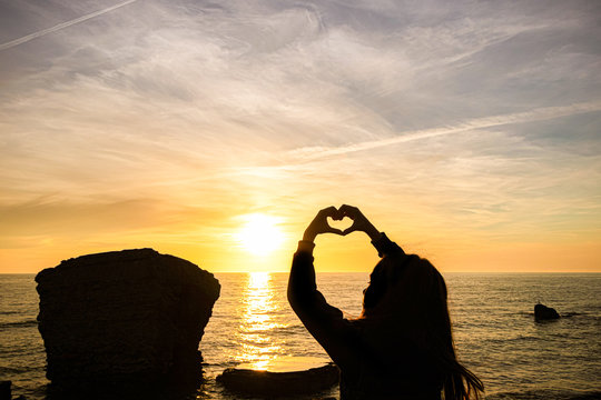 girl silhouette on sunset sea background. the girl depicts a heart from her hands.