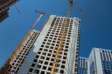 White high-rise building under construction and tower cranes against the blue sky.