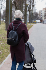 Girl walks in the park with a baby carriage.