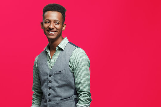 Laugh a cheerful guy in casual clothes, standing and smiling, isolated on a raspberry color background. Copy space.