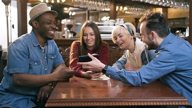 Four happy caucasian friends using smart phone together in the bar, pub.