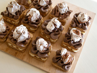 Portion cakes of meringue and cocoa butter cream in square form on a wooden stand, a piece of cake on a light wooden background. Restaurant serving. Selective focus, close up