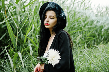 Sensual smoker girl all in black, red lips and hat. Goth dramatic woman hold white chrysanthemum...