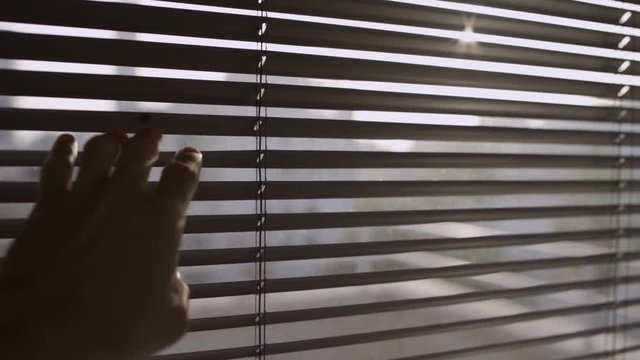 Pulling down on a window blind or shutter in order to look outside
