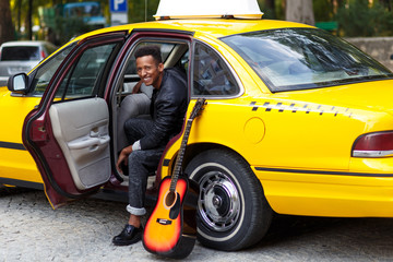 A smiling young man in car with opened door of yellow car, looking and smiling, with left leg...