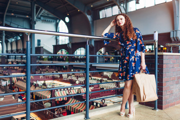 Young happy woman holding shopping paper bags in shopping center and waiting for friends.