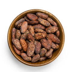 Roasted unpeeled cocoa beans in a brown wooden bowl isolated on white from above.