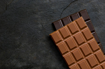 A slab of milk chocolate on top of a slab of dark chocolate on black slate from above. Space for...