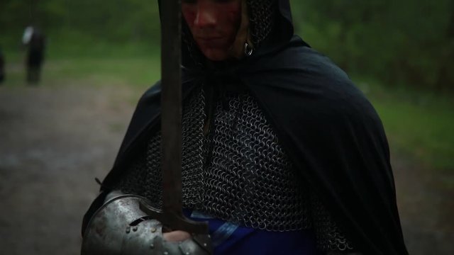 Portrait of young man in the image of a medieval knight in chain armor and with a sword in his hands in the evening.