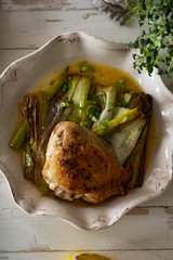 Roasted skin-on chicken thighs with leek and wine sauce on white distressed wooden table