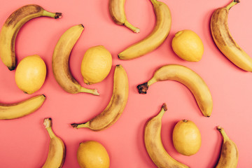 Top view of bright juicy lemons and yellow bananas on coral background