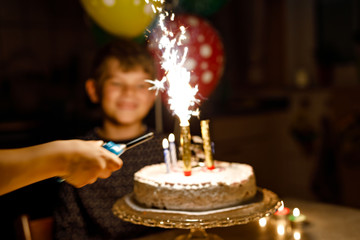 Adorable happy blond little kid boy celebrating his birthday. Child blowing candles on homemade baked cake, indoor. Birthday party for school children, celebration of 8 years. Selective focus.