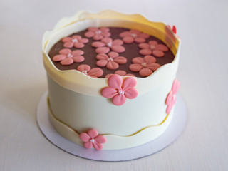 Cake with a chocolate decor - chocolate white boards and pink chocolate flowers. Cake for birthday, anniversary and any other holiday. White background, isolated. Selective focus, close up.