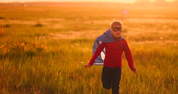 A boy in a suit and a superhero mask running across the field at sunset on the grass