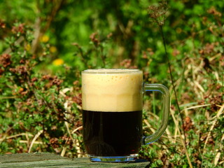 Mug of dark frothy beer on table in spring garden