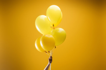 cropped view of woman holding festive bright minimalistic decorative balloons on yellow background