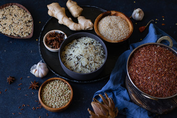 Various types of rice and grains with spices on blue background. Brown rice and mixed wild rice.