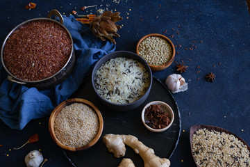 Various types of rice and grains with spices on blue background. Brown rice and mixed wild rice.