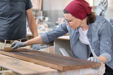 Middle-aged craftswoman working in woodworking workshop. Female varnishing wooden board with oil, varnish.