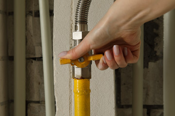 Woman turning on or turning off gas supply on yellow gas pipe