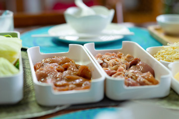 Marinated chicken meat and marinated pork on a white plastic tray in a Japanese shabu-shabu set which is placed on a wooden table