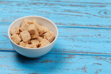 Brown cane sugar cubes on blue wooden background