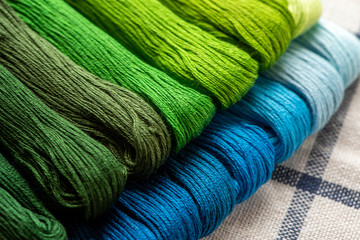 Blue and green threads for embroidery arranged in a row. Hobbies, background, selective focus.