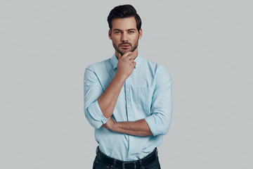 What if... Handsome young man looking at camera and keeping hand on chin while standing against...