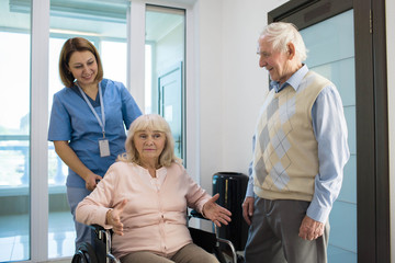 Fototapeta premium senior woman in wheelchair talking with nurse in a hospital behind her standing senior husband.