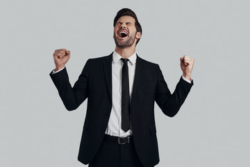 Successful man. Handsome young man in full suit gesturing and shouting while standing against grey background