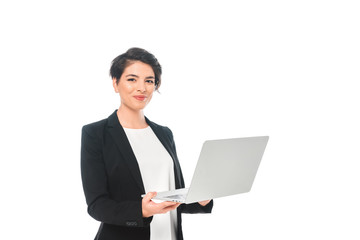 cheerful mixed race businesswoman holding laptop and smiling at camera isolated on white