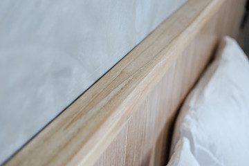 Light wooden bedhead, grey concrete wall, white bed sheets. Minimal loft design, flat interior details