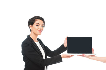 partial view of woman taking laptop with blank screen from smiling mixed race businesswoman isolated on white