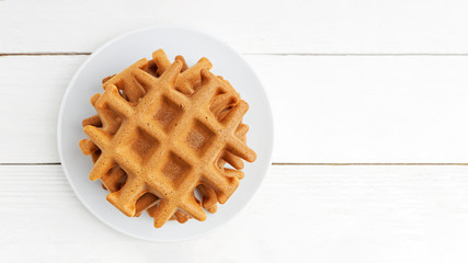 Stack of homemade soft belgian waffles on white wooden table. Top view. Copyspace.