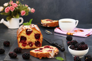 Cupcake with blackberries is located on a white plate on a dark background, section of the cake in the foreground