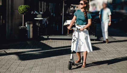 Fototapeta na wymiar young woman on a white electric scooter in sunglasses walks around the city on a sunny day.