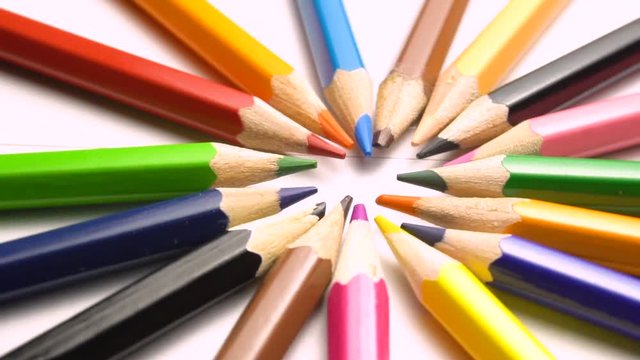 Colored pencils laid out in a circle by the colors of the rainbow on a light background