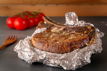 Meat steak baked in foil on a wooden table with fresh tomatoes. Close-up