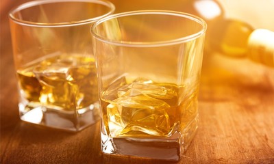 Glasses of Whiskey and Ice with Bottle on Background