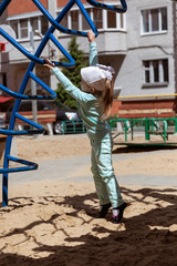 A little, pretty, active girl plays on the playground on a sunny day.